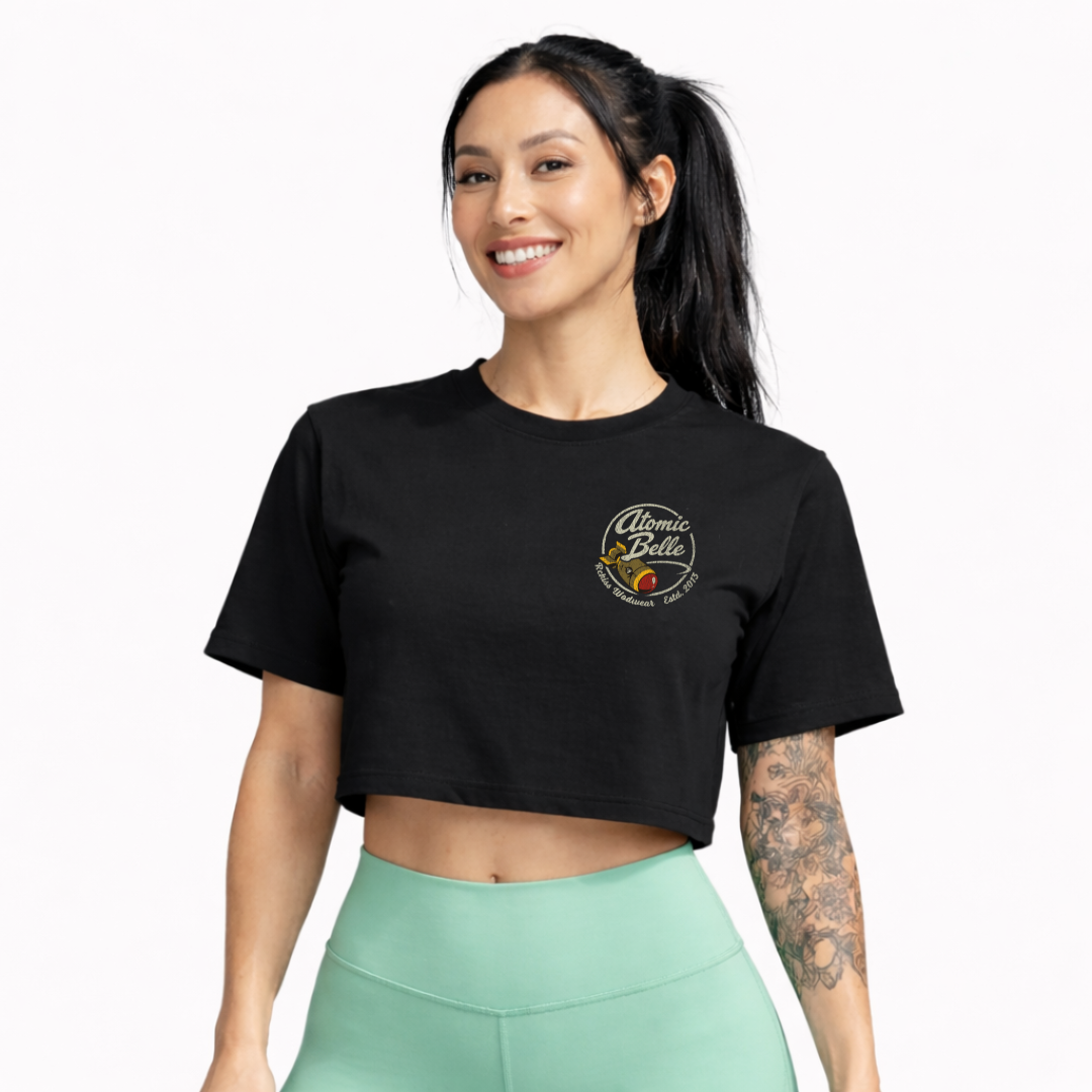 Modelo mujer con crop top Atomic Belle Rckiss, vista frontal sonriendo con leggins verde menta, tatuajes florales, mujer fitness gym