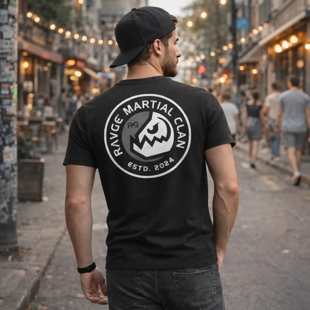 Modelo hombre con playera RVG Martial Clan RAVGE, vista trasera en calle urbana con gorra, diseño emblema guerrero, ropa MMA streetwear
