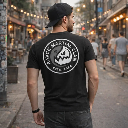 Modelo hombre con playera RVG Martial Clan RAVGE, vista trasera en calle urbana con gorra, diseño emblema guerrero, ropa MMA streetwear